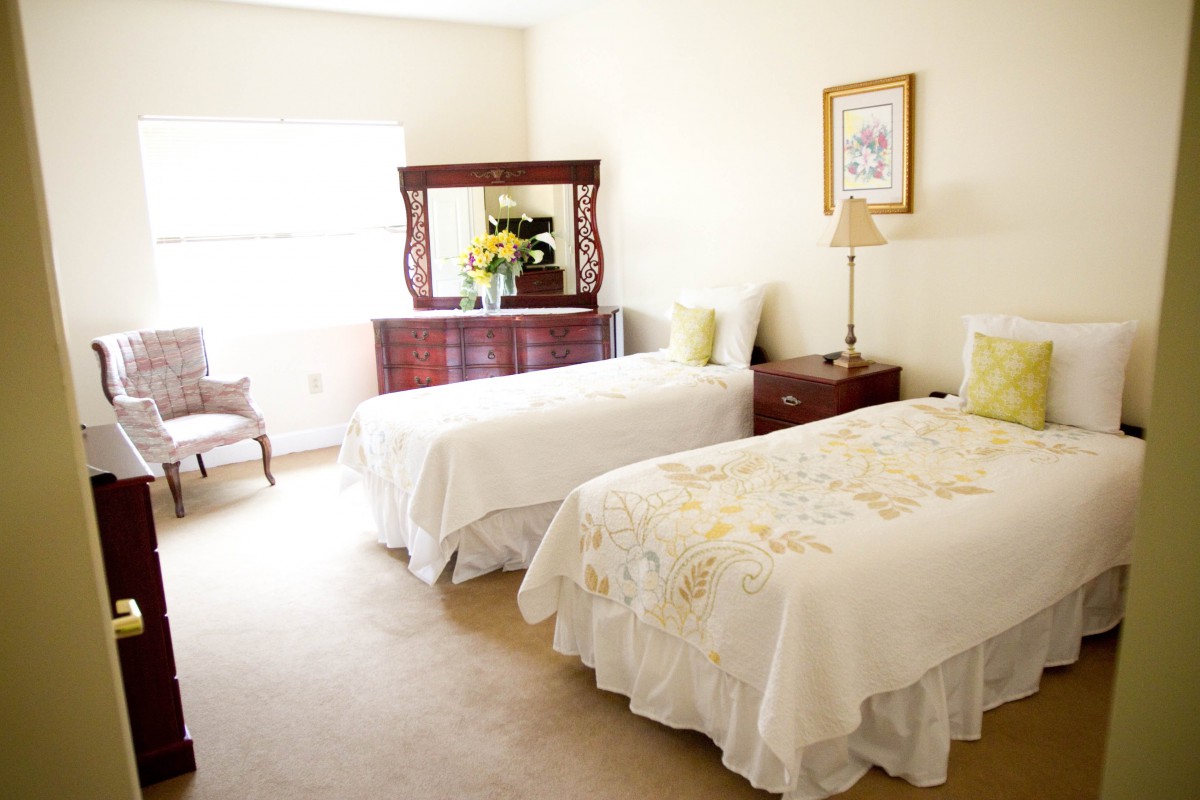 A cozy bedroom with two twin beds, a dresser with a mirror, and soft lighting.