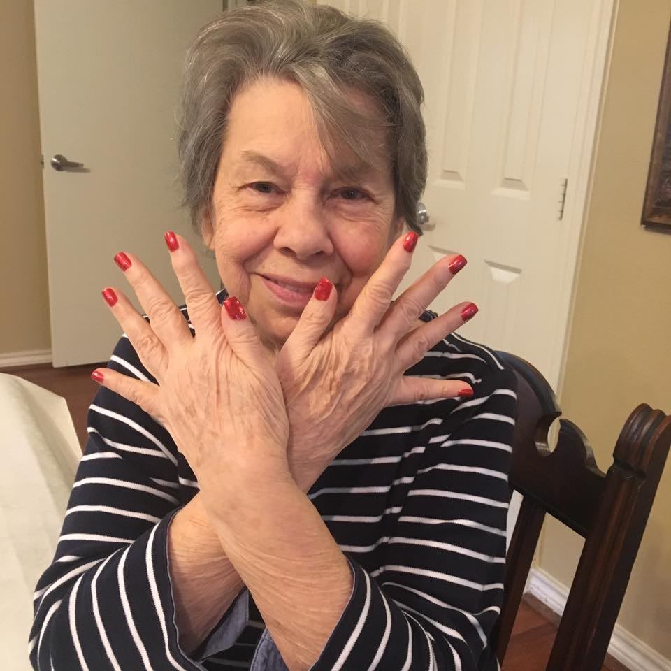 A smiling woman with red-painted nails poses indoors.