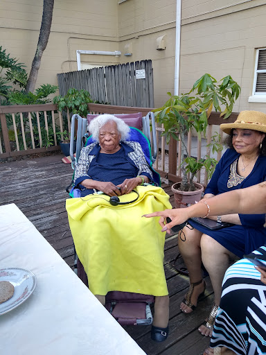 A heartfelt family gathering outdoors, featuring an elderly woman in a wheelchair surrounded by loved ones.
