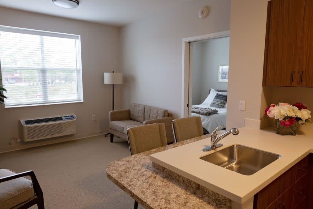 A view of a modern apartment with an open living area, kitchen counter, and cozy bedroom.