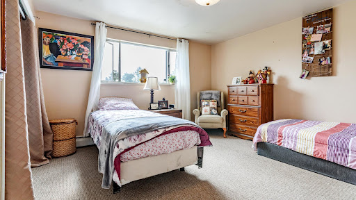 A cozy bedroom featuring two beds, a wooden dresser, and plenty of natural light.