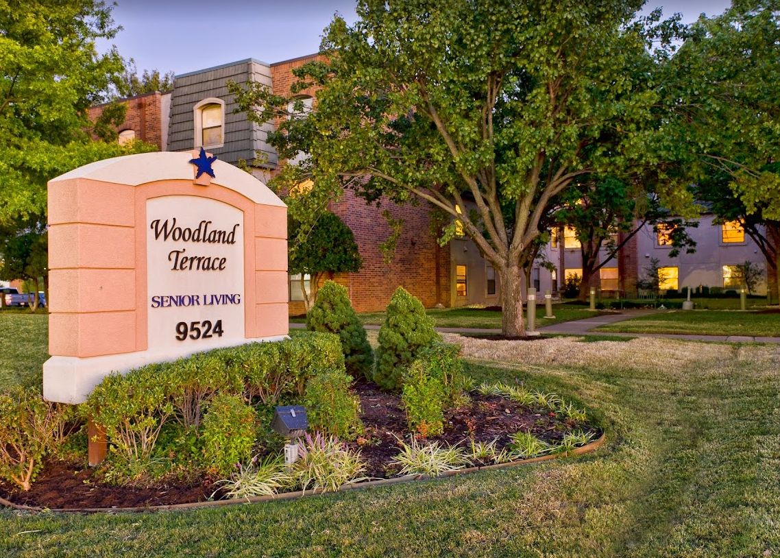 Entrance sign for Woodland Terrace apartment complex surrounded by lush landscaping.