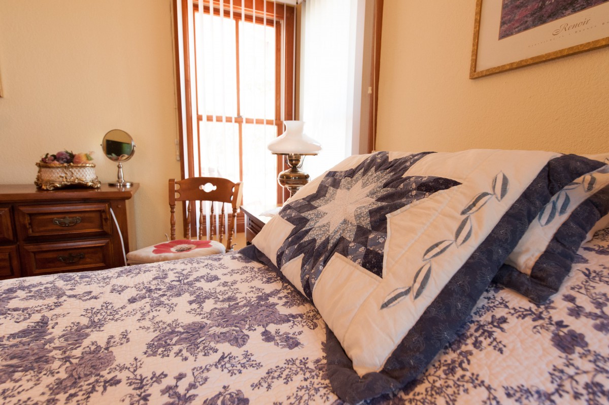 A cozy bedroom featuring a quilt with a star pattern, a wooden chair, and a lamp near the window.