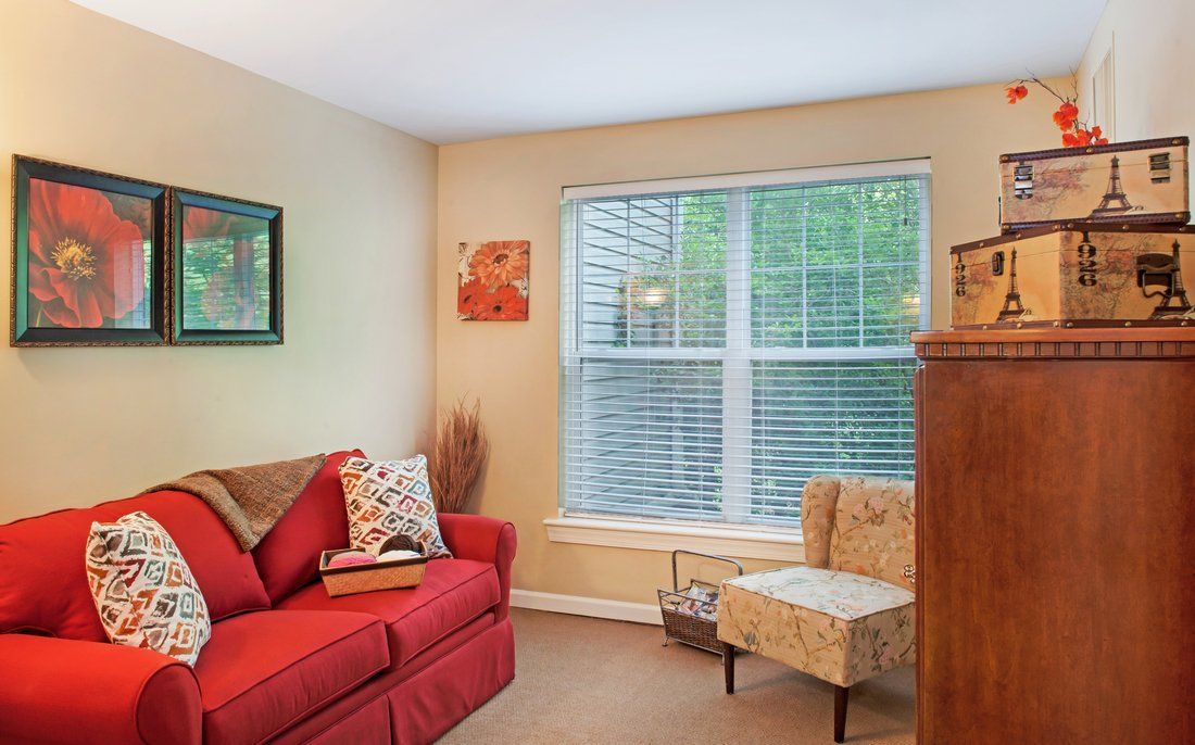 A cozy living room with a red sofa, an armchair, and a large window.