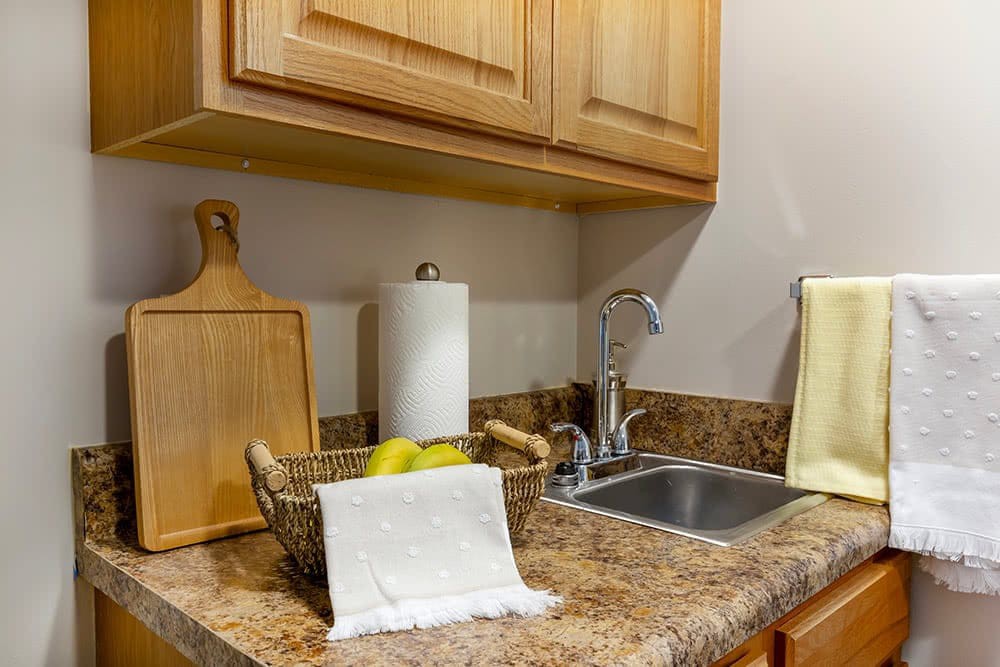 A neat kitchen countertop with a sink, wooden cabinets, and a fruit basket.