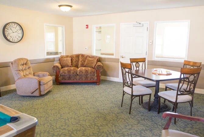 A cozy living room with a sofa, chairs, and a table on a green carpet.