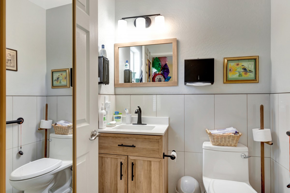 A well-lit bathroom featuring a wooden vanity, mirror, and toilet with decorative artwork on the walls.