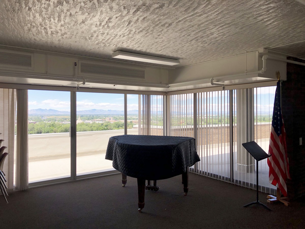 A room with large windows showcasing a mountain view, featuring a covered grand piano and a music stand.