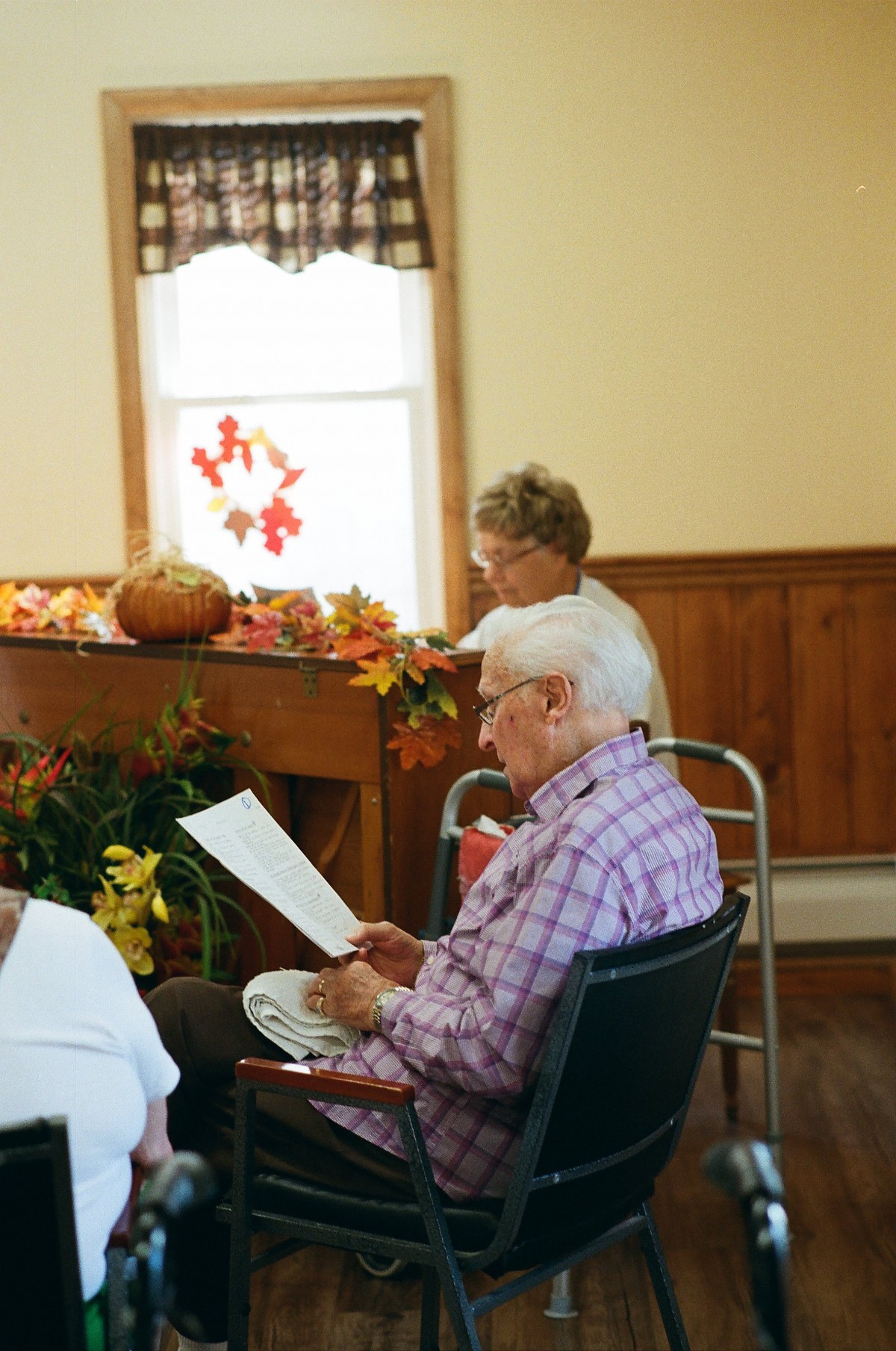 Elderly individuals engaged in reading during a community gathering with autumn-themed decorations.