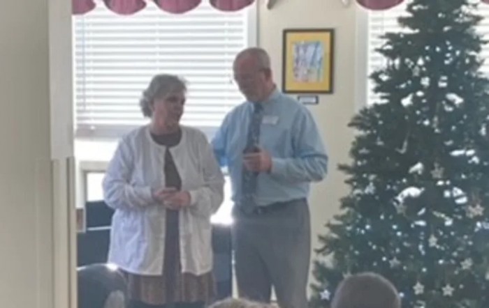 Two people speaking at an indoor event near a Christmas tree.