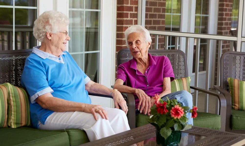Two elderly women enjoying a conversation on a porch.