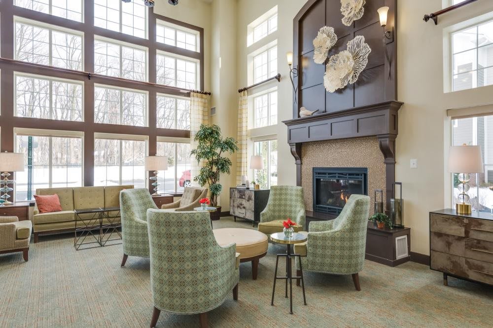 A cozy living room with large windows, armchairs around a round table, and a fireplace adorned with floral decorations.