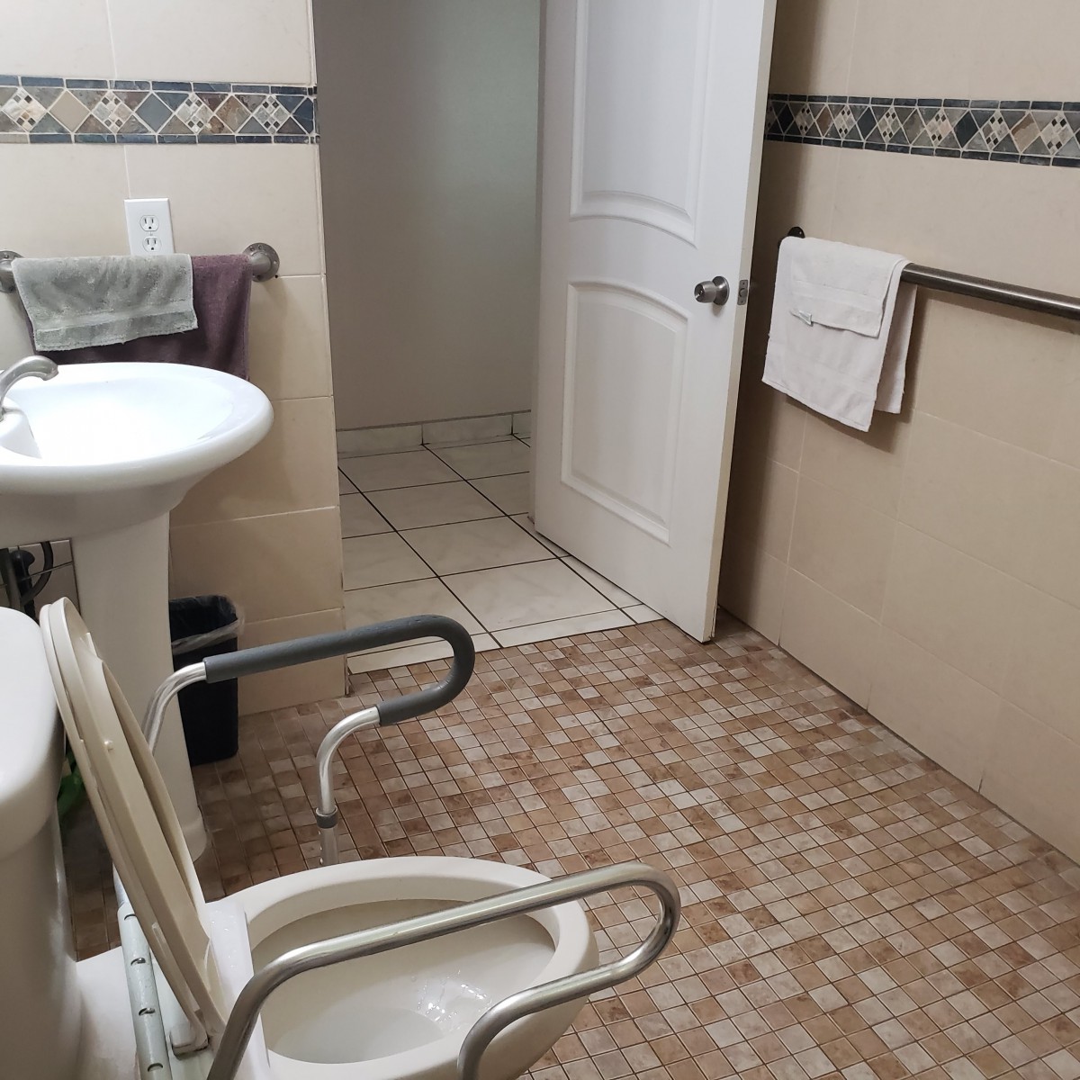 An accessible bathroom featuring a toilet with grab bars and a pedestal sink.