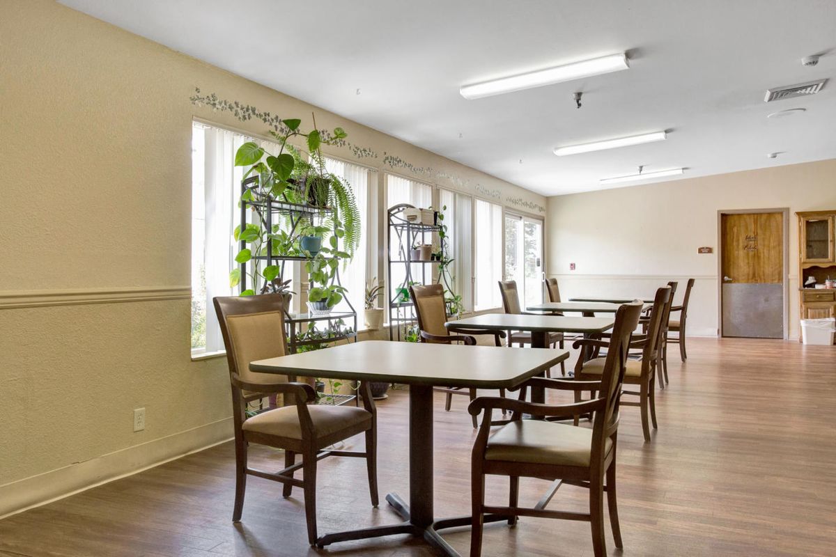 A spacious dining area with several tables and chairs, featuring large windows and green plants.