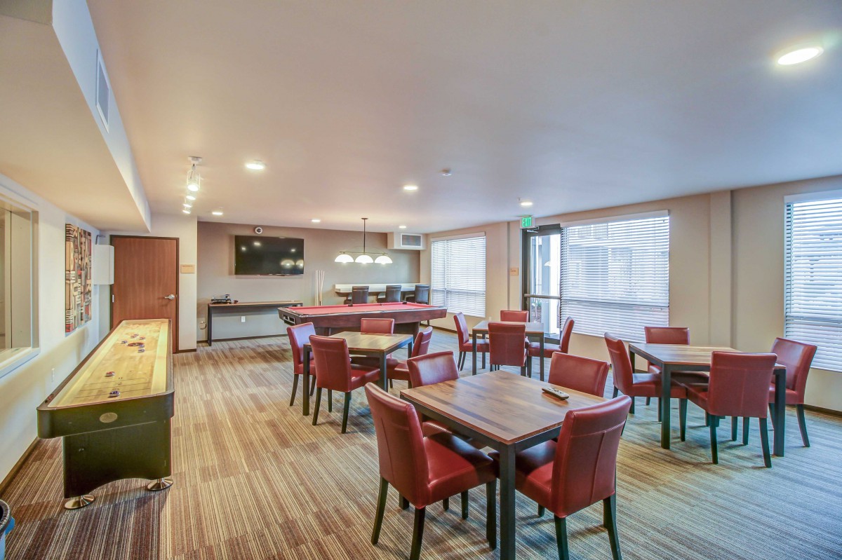 A modern dining area with red chairs and wooden tables, featuring a mounted television and warm lighting.