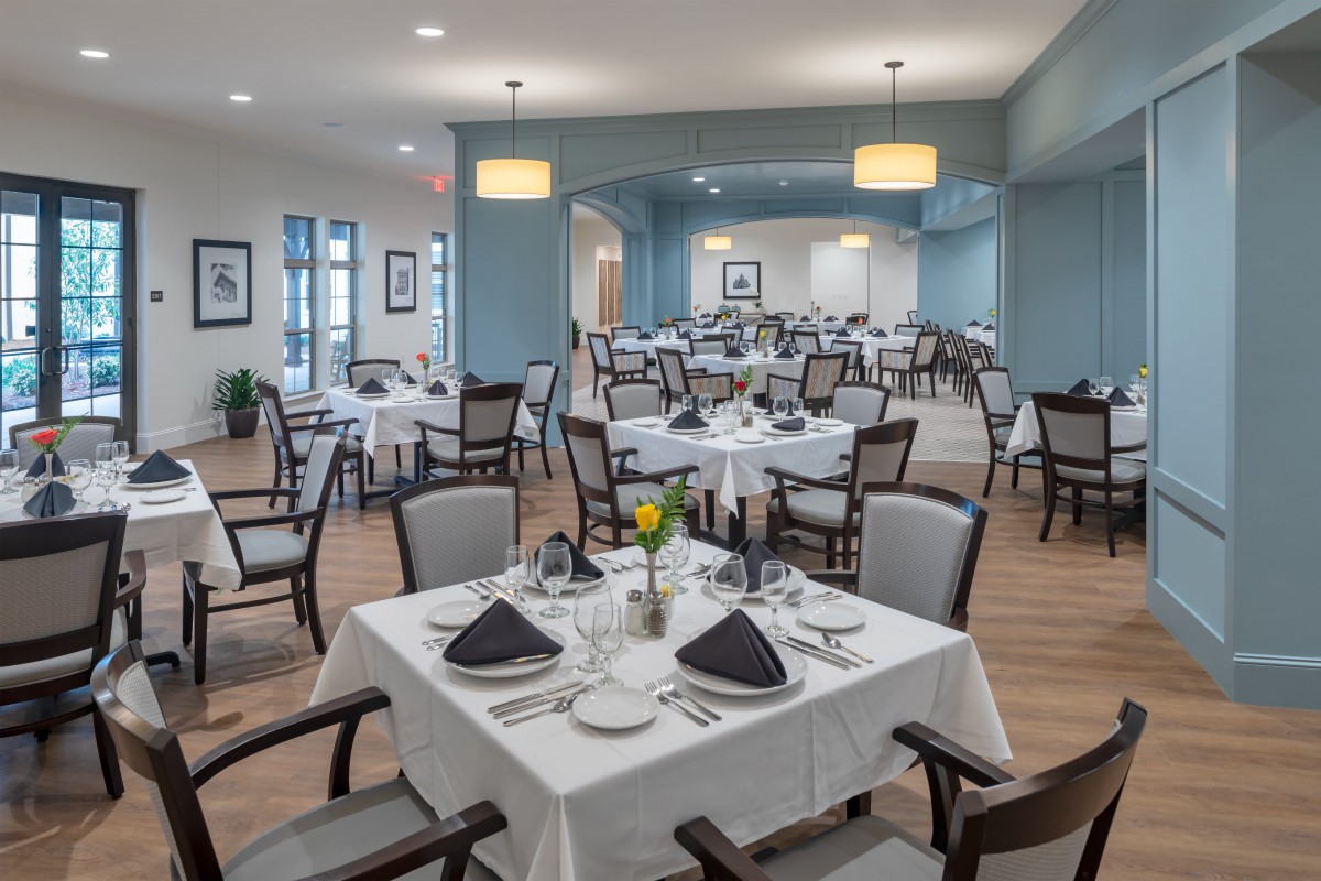 A spacious, elegantly set dining room with neatly arranged tables and chairs.
