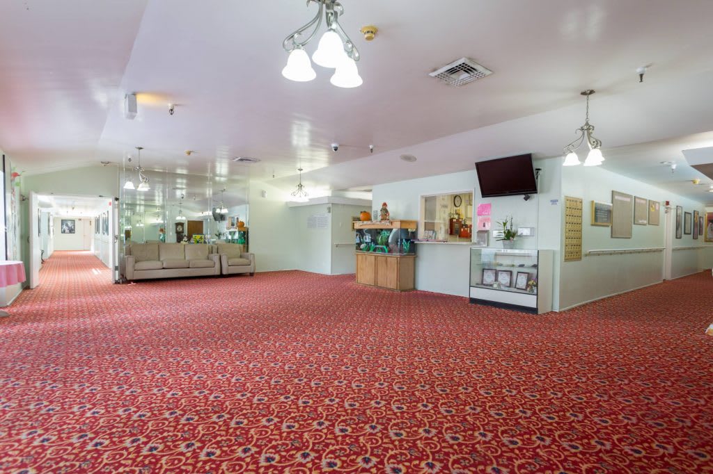 A spacious lobby area featuring red carpet, comfortable seating, mirrors, and a wall-mounted television.
