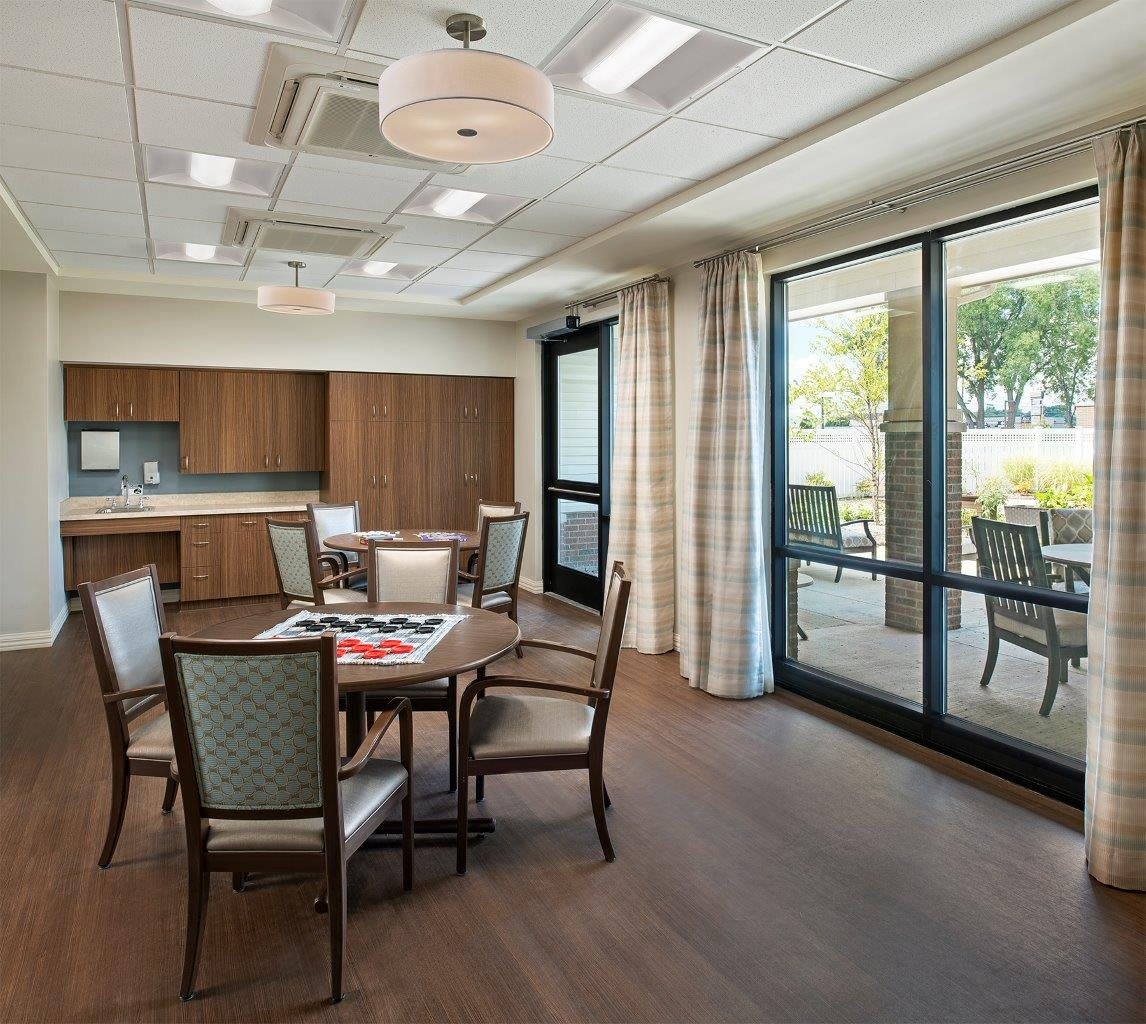 A modern dining room with a set of tables and chairs, featuring large windows with curtains and wood flooring.