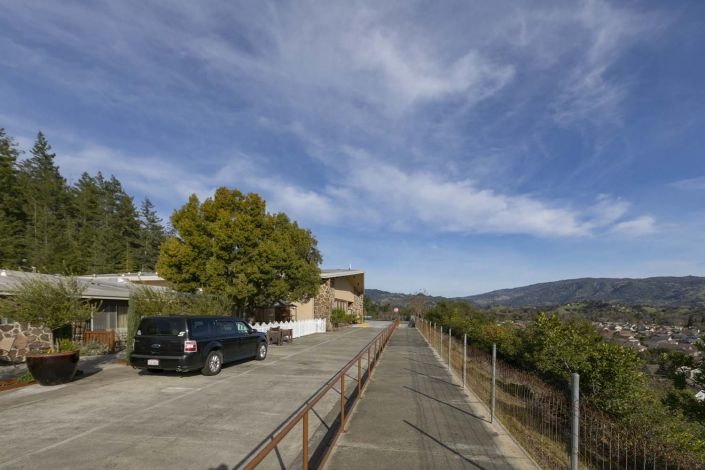 A scenic outdoor pathway with a car parked beside trees and a building under a partly cloudy sky.
