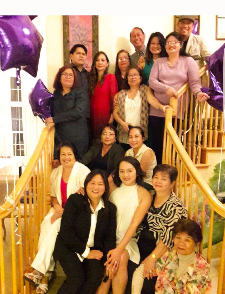 A group of people gathered on a staircase for a family event, surrounded by purple balloons.