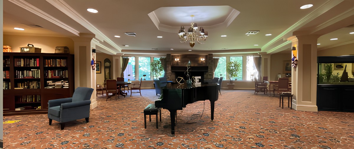 An elegant music room featuring a grand piano and chandelier, with large windows providing natural light.
