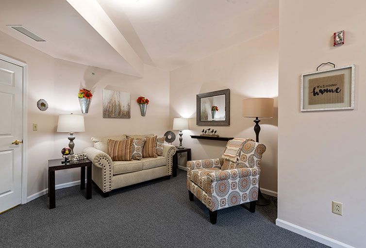 A cozy living room with a sofa, patterned armchair, and elegant decor featuring lamps and a wall mirror.