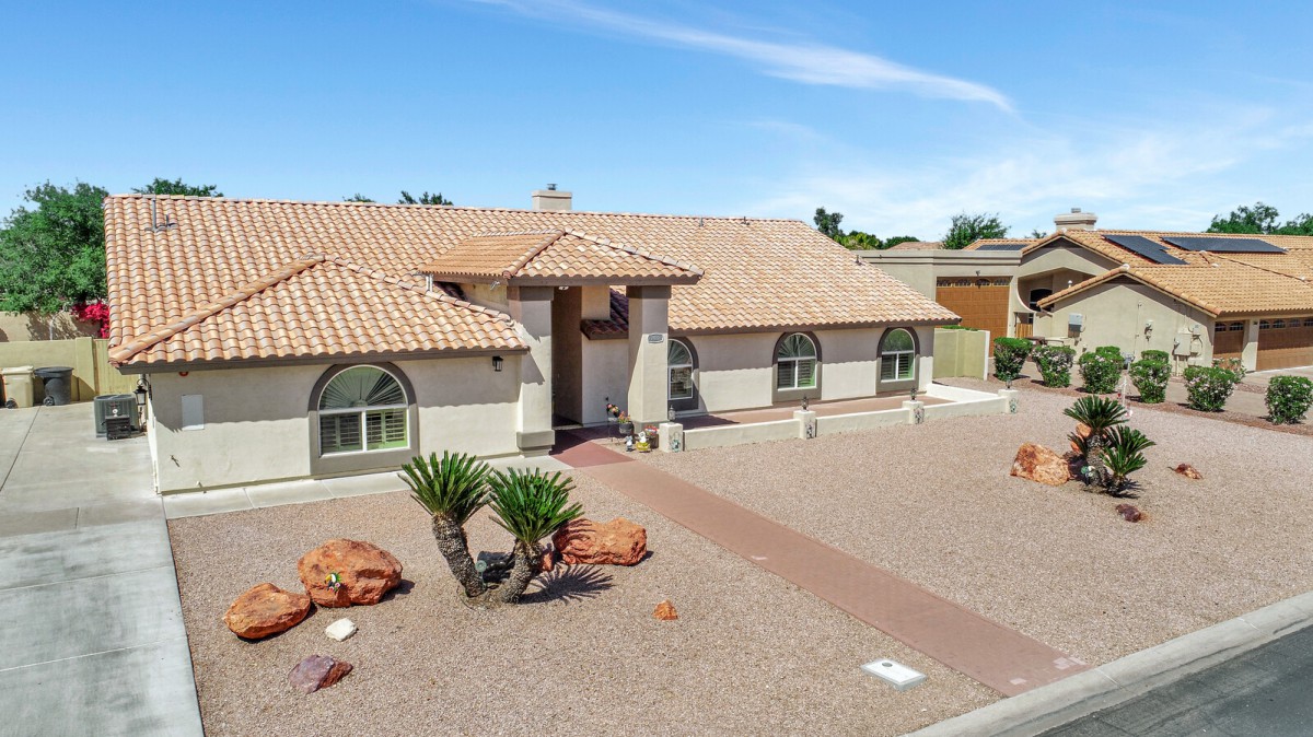 A single-story house with a desert landscape featuring rocky terrain and native plants.