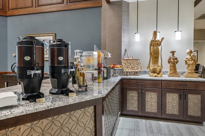 A modern hotel self-serve coffee station with beverage dispensers and decorative elements on a patterned countertop.