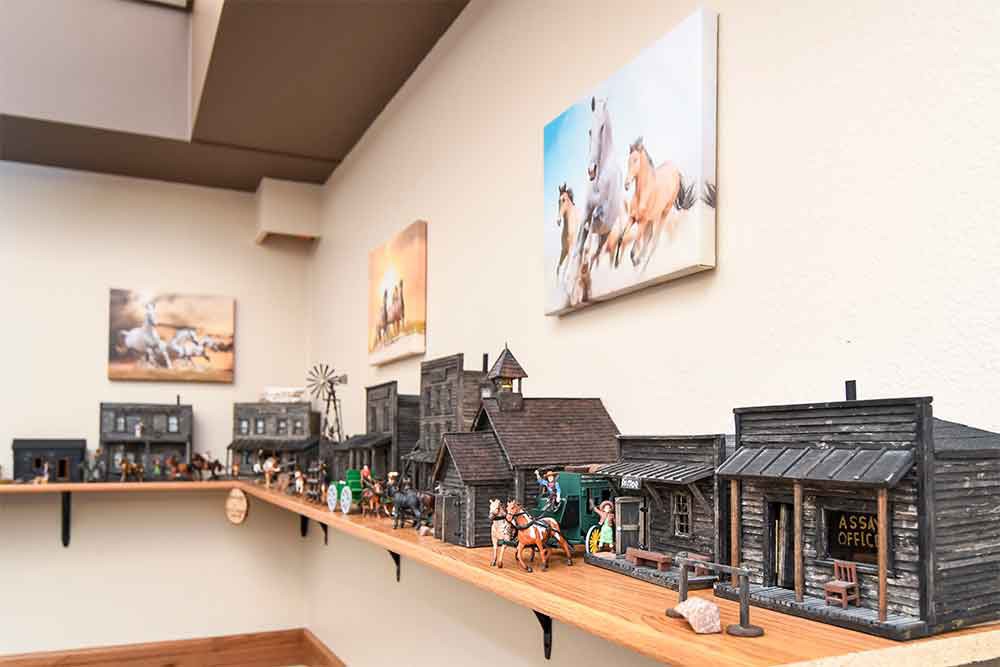 A detailed miniature model of a western-style town displayed on a shelf, accompanied by artwork on the walls.