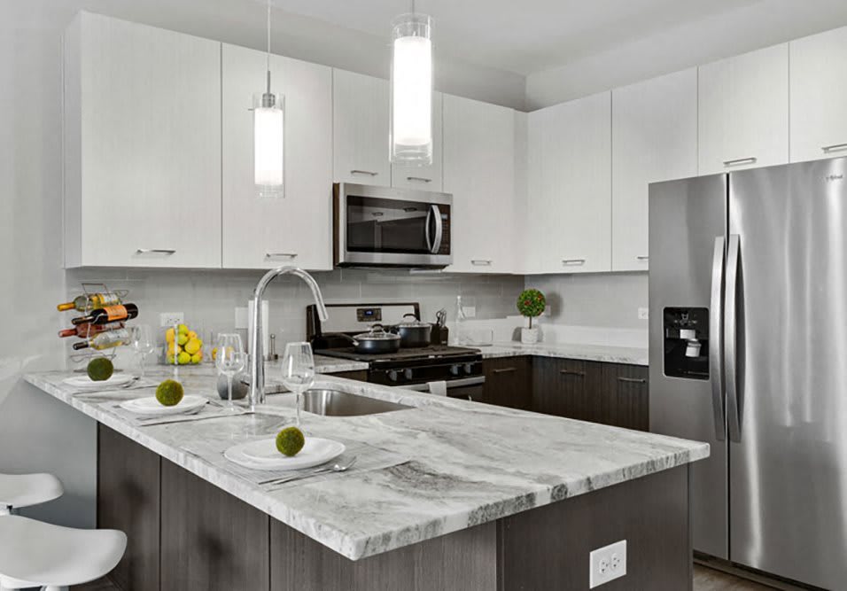A modern kitchen with white cabinets, stainless steel appliances, and a marble countertop island.