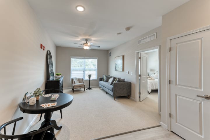 A modern living room with a sofa and table, featuring neutral colors and ample natural light.