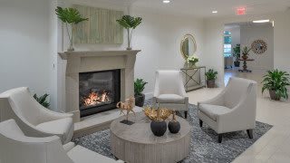 A cozy and modern living room featuring a comfortable seating area with white chairs, a round wooden coffee table, and a warm fireplace surrounded by elegant decor and green plants.