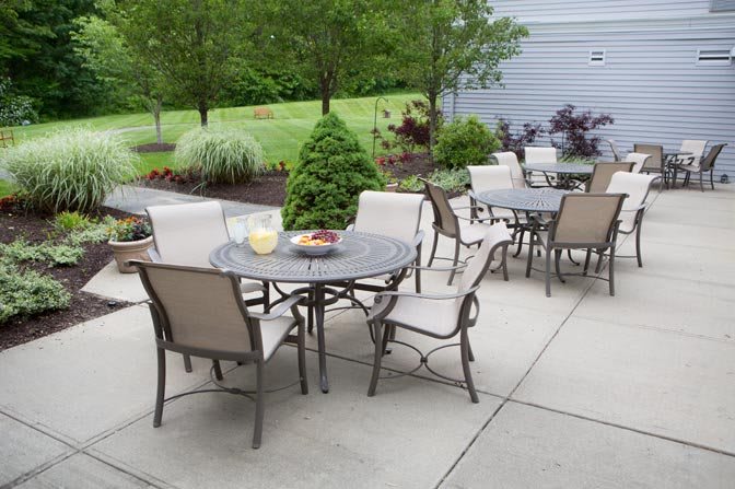 An outdoor patio setup with tables and chairs on a paved area surrounded by a garden.