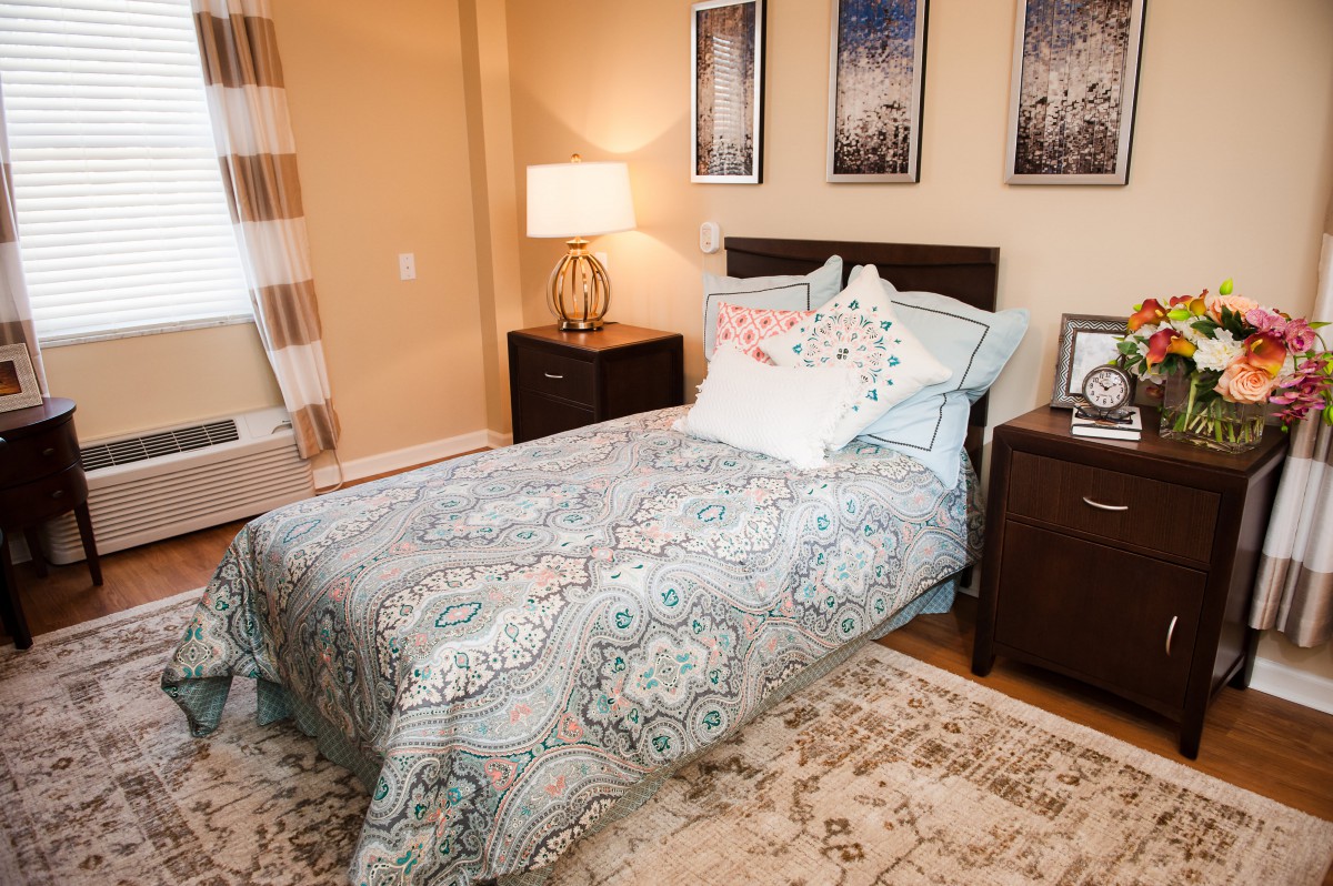 A cozy bedroom featuring a neatly made bed with patterned bedding, flanked by two nightstands with lamps, and adorned with wall art.