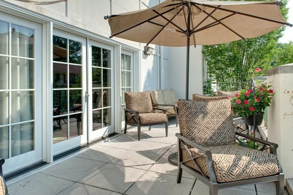 A sunny patio with comfortable chairs and an umbrella, next to a set of glass doors.