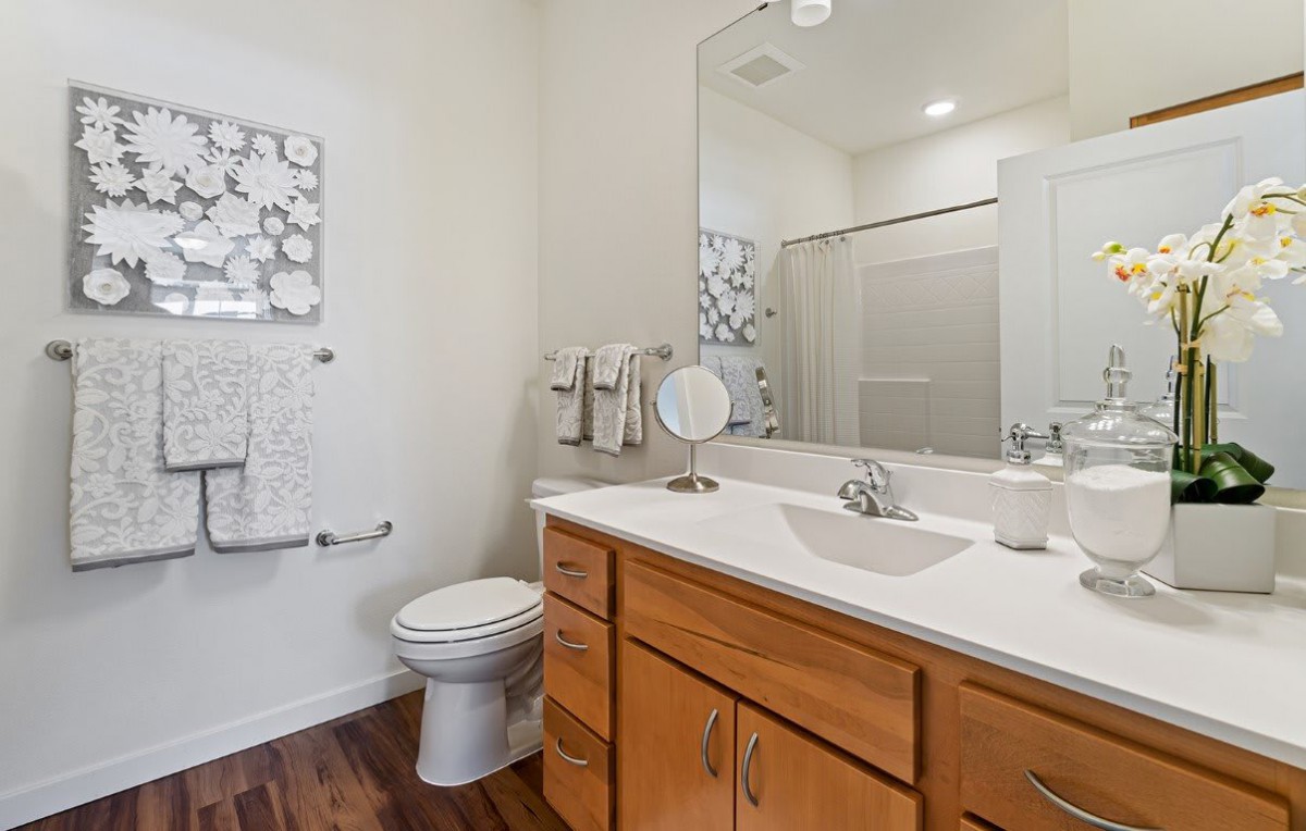 A clean and modern bathroom with a sink, mirror, toilet, and wooden cabinets.