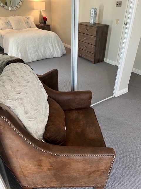 A cozy bedroom with a brown leather chair, mirror sliding doors, and a neatly made bed.