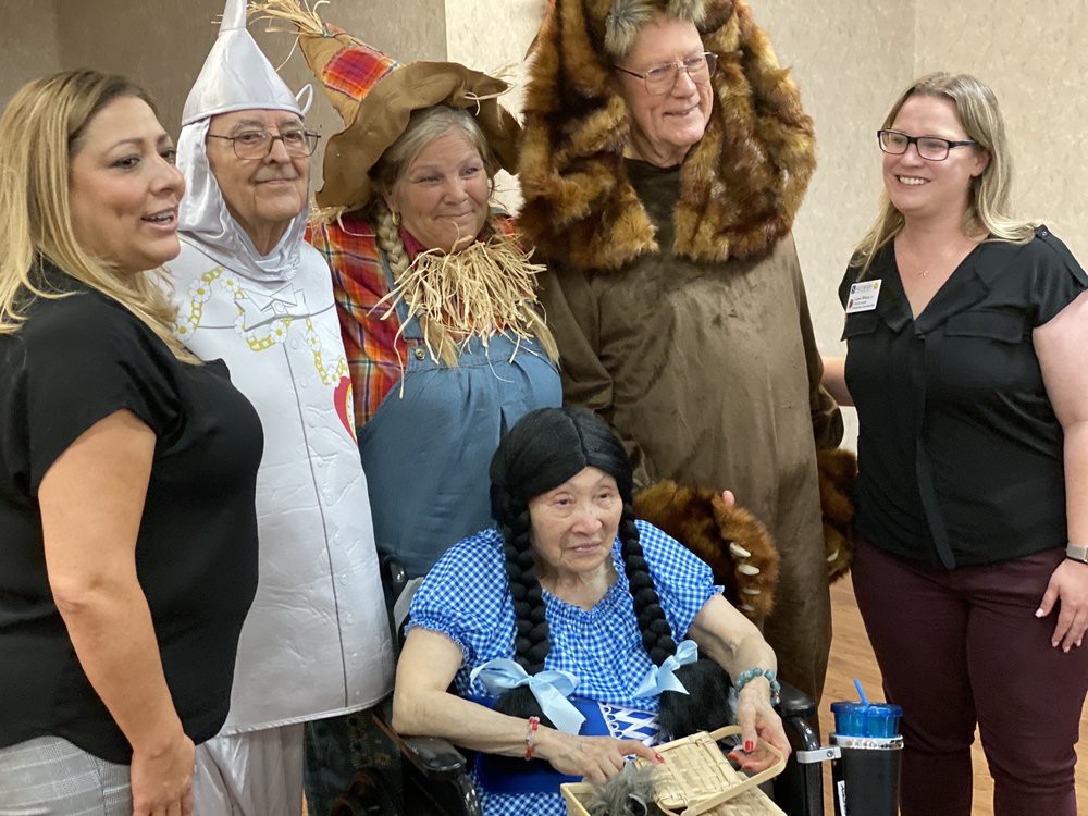 A group of people dressed in Wizard of Oz costumes posing for a fun group photo with an elderly woman.