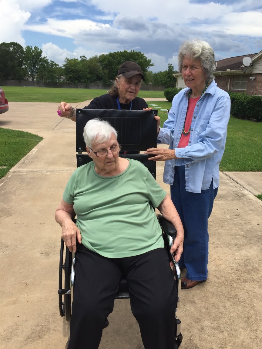 Elderly person in a wheelchair with two caregivers outside.
