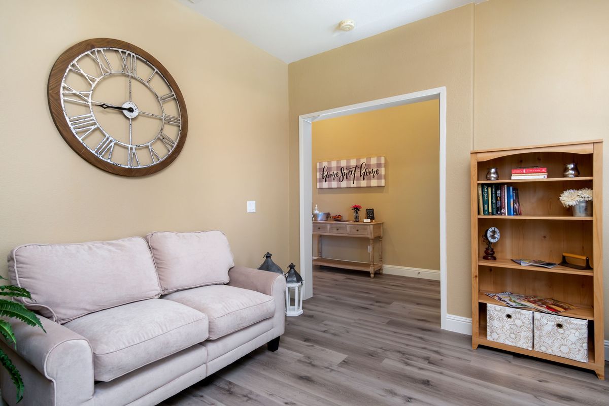 A cozy living room with a beige couch, a large wall clock, and wooden flooring.