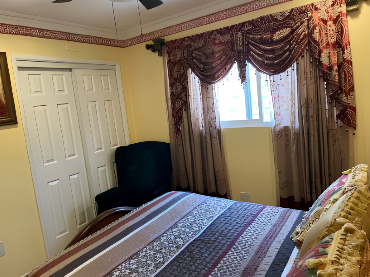 A cozy bedroom with striped bedding, ornate curtains, and a ceiling fan.