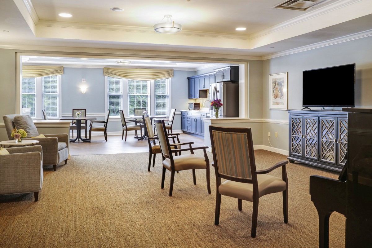 A spacious and well-lit seating area with several chairs and tables, featuring a carpeted floor and large windows.