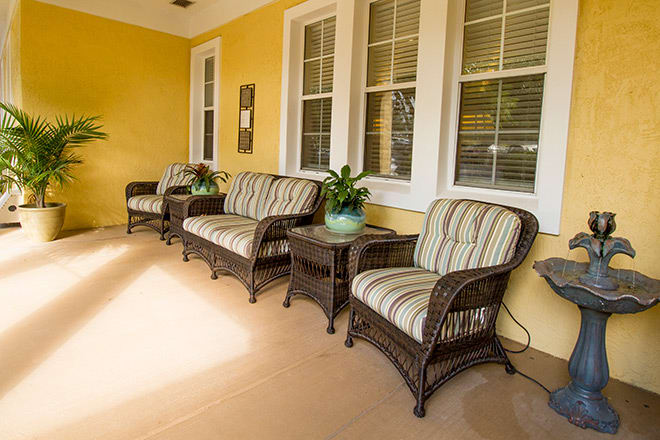 A cozy porch with wicker furniture and striped cushions against yellow walls.