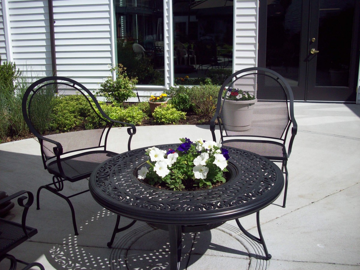 A cozy outdoor patio area with a decorative iron table and chairs, featuring a floral centerpiece.