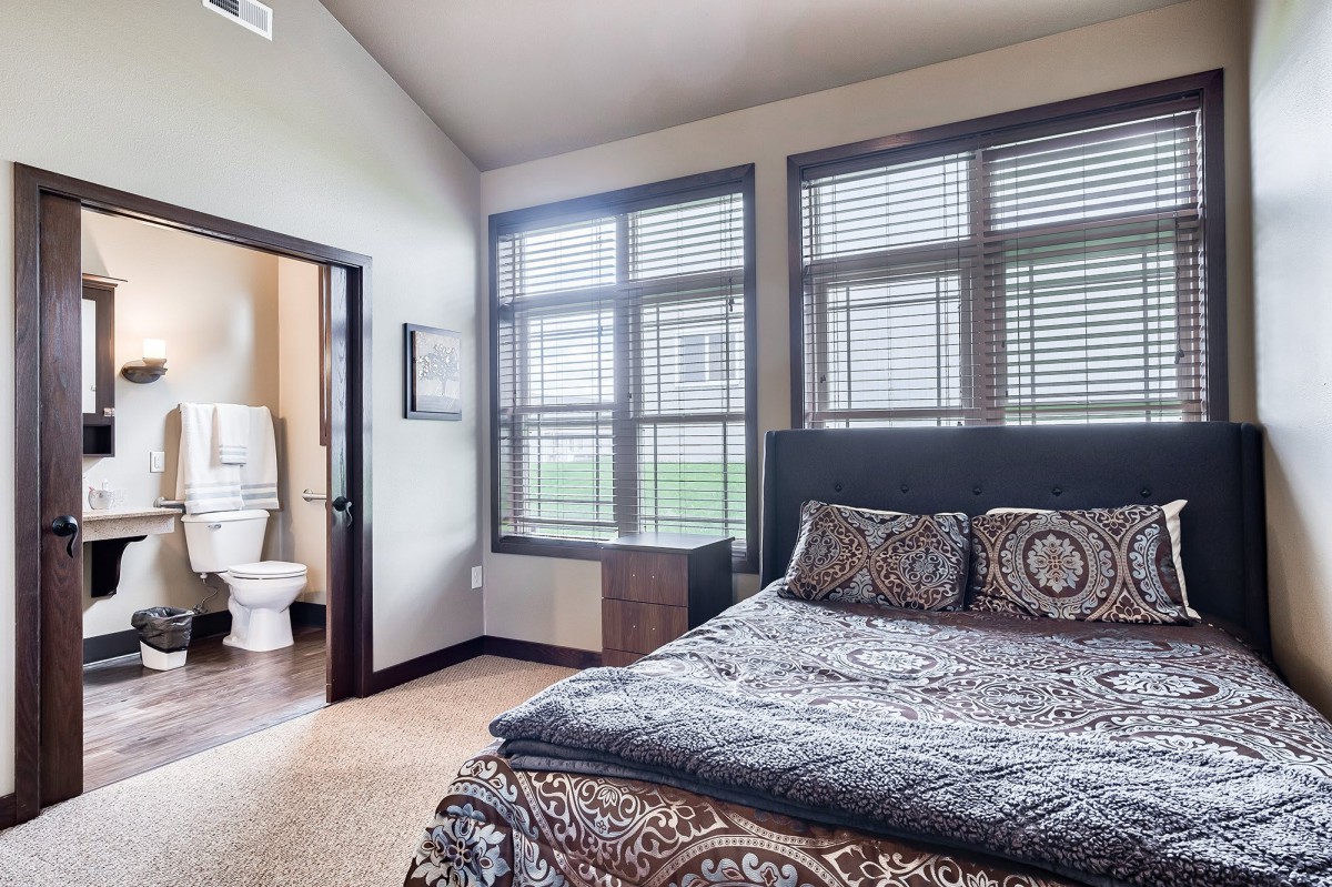A modern bedroom with large windows and a view into an adjoining bathroom.