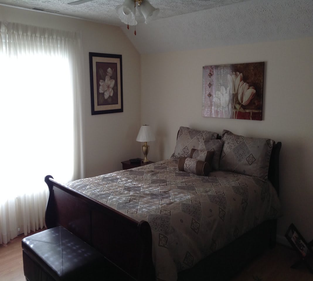 A cozy bedroom with a neatly made bed, artwork on the walls, and soft natural light.