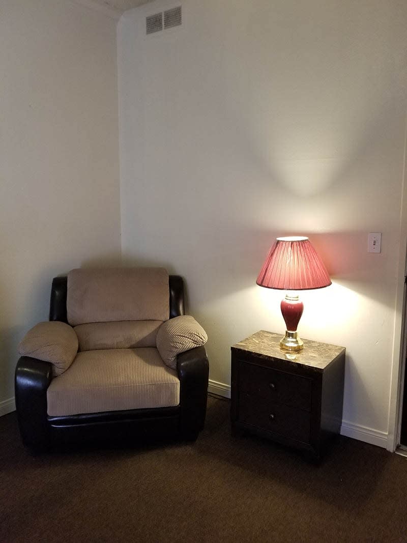 A cozy armchair next to a lamp on a side table in a living room corner.