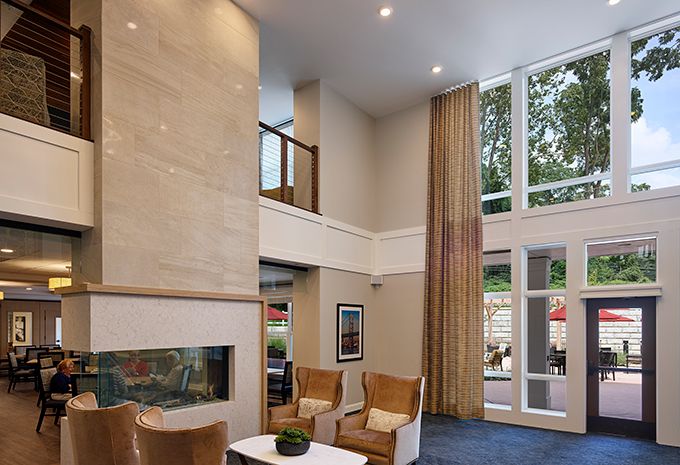 A modern living room with high ceilings, large windows, and comfortable seating around a fireplace.