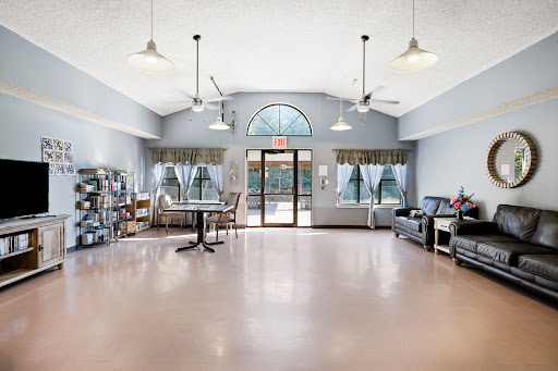 A spacious and bright lounge area featuring comfortable seating, tables, and large windows for natural light.