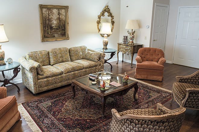 A vintage-style living room featuring a patterned sofa, armchair, ornate mirror, and a classic coffee table atop a decorative rug.